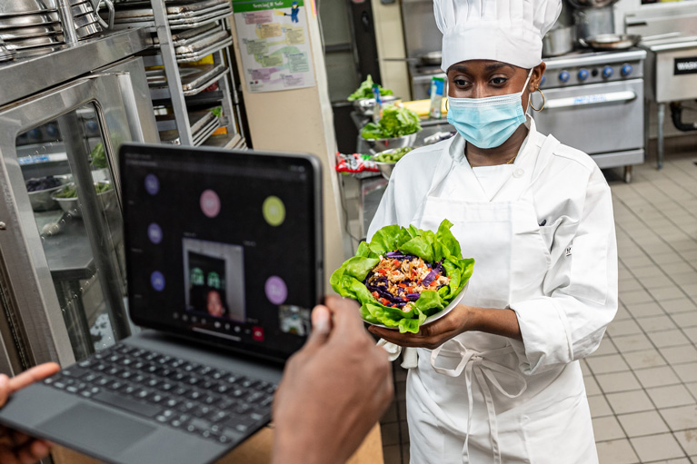 Student chef showing meal to instructor on computer