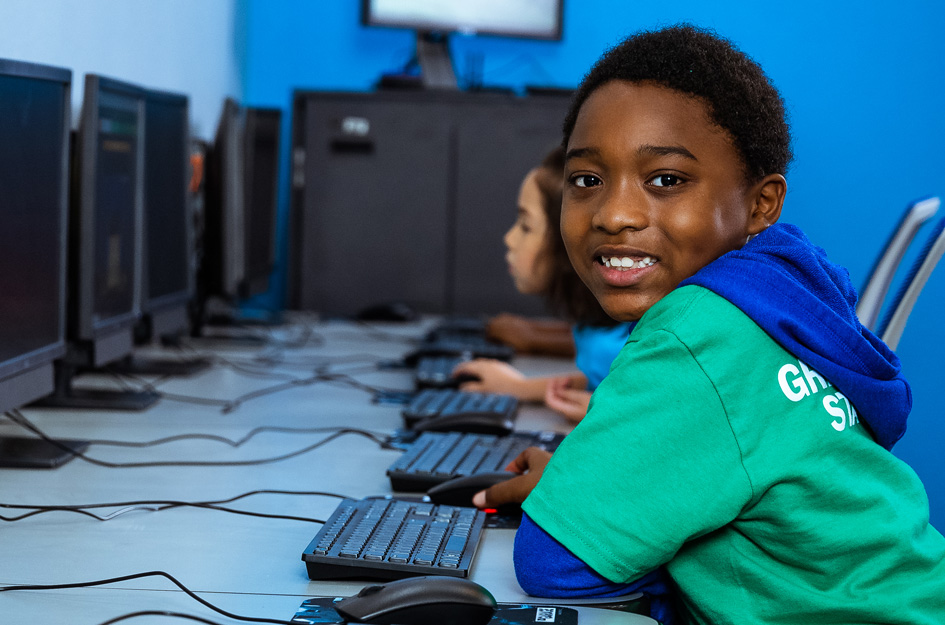Boy smiles from chair in computer lab