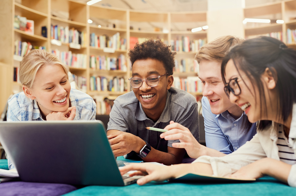 4 diverse teens looking at laptop in library