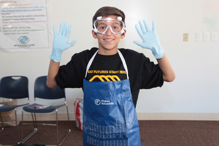 Young boy wearing Fisher Scientific chemist apron, goggles and gloves