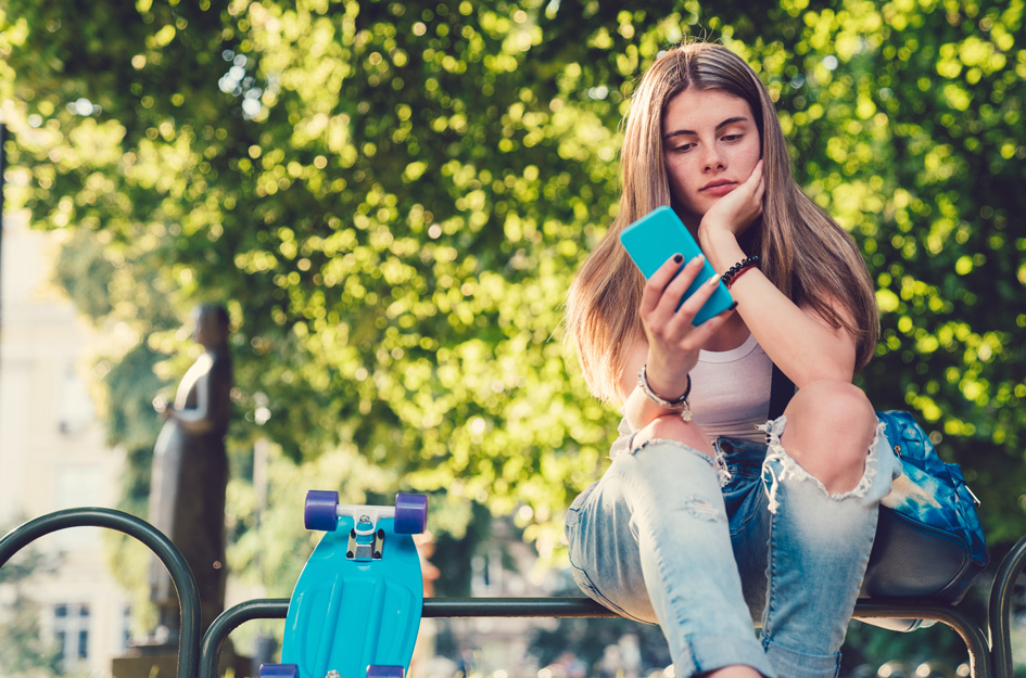 Teen girl outdoors on bench, looking at cell phone